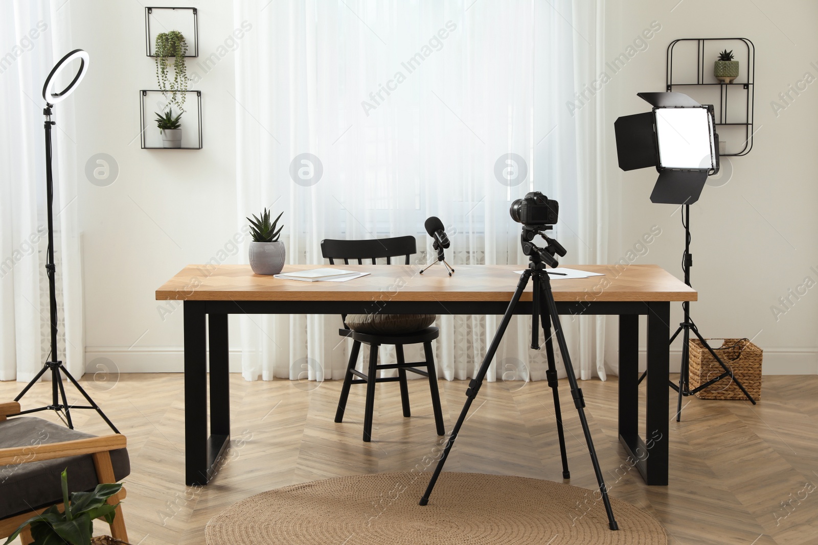 Photo of Camera and lighting equipment on tripods near table in room. Blogger workplace