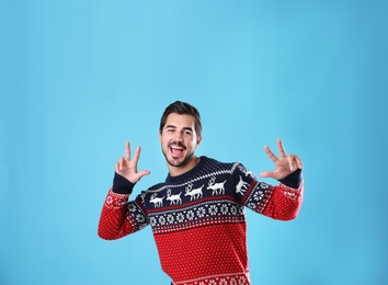 Portrait of happy young man in Christmas sweater on light blue background