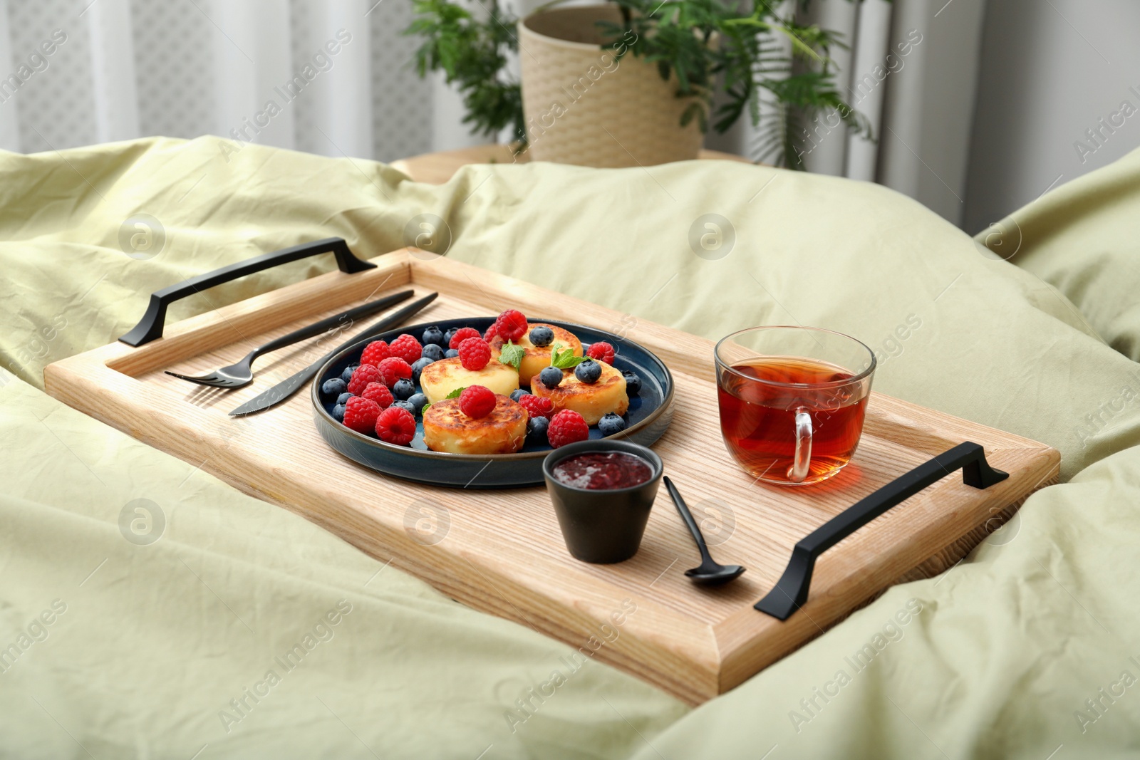 Photo of Tasty breakfast served in bedroom. Cottage cheese pancakes with fresh berries and mint on wooden tray