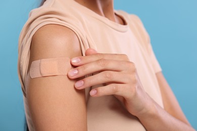 Photo of Woman with sticking plaster on arm after vaccination against light blue background, closeup