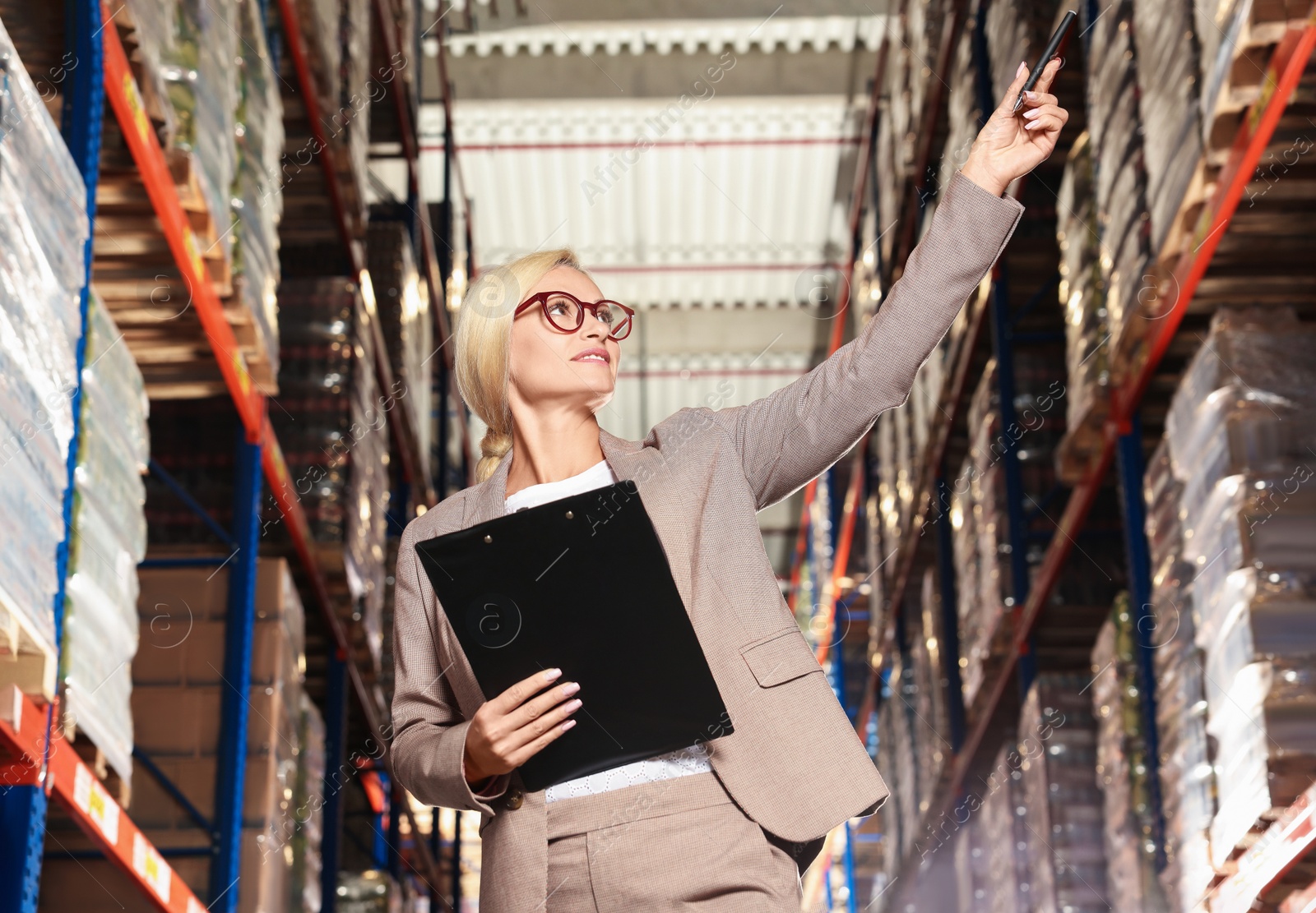 Photo of Happy manager holding clipboard in warehouse with lots of products, low angle view