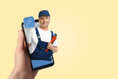 Image of Find plumber. Man using mobile phone on light yellow background, closeup. Specialist looking out of gadget