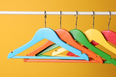 Photo of Bright clothes hangers on metal rail against yellow background