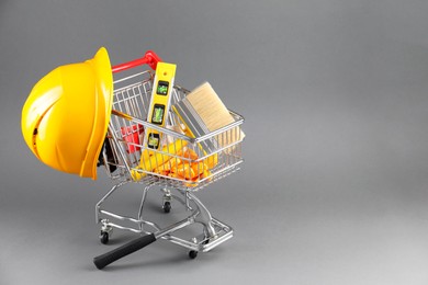Photo of Small shopping cart with construction level, brush, gloves and hard hat on grey background. Space for text