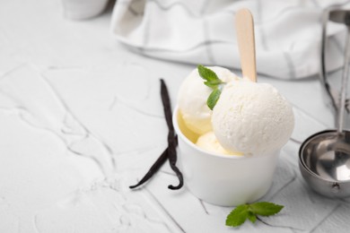 Photo of Delicious ice cream with mint and vanilla pods on white textured table, closeup. Space for text