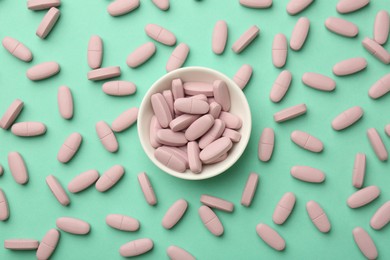 Photo of Pink vitamin capsules and bowl on turquoise background, flat lay