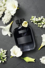 Bottle of luxury perfume and floral decor on black table, flat lay