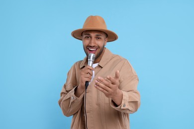Photo of Handsome man with microphone singing on light blue background