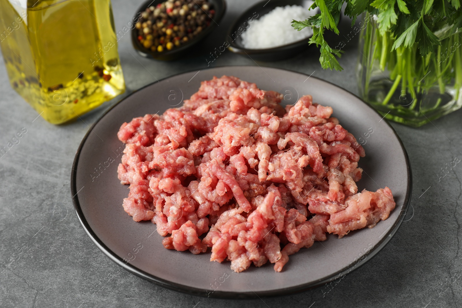 Photo of Raw ground meat, spices, parsley and oil on grey table