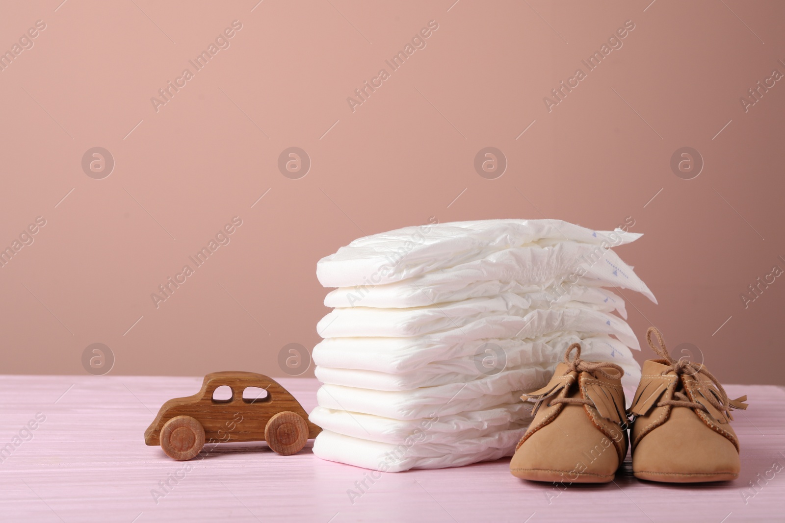 Photo of Baby diapers, toy car and child's shoes on wooden table against pink background