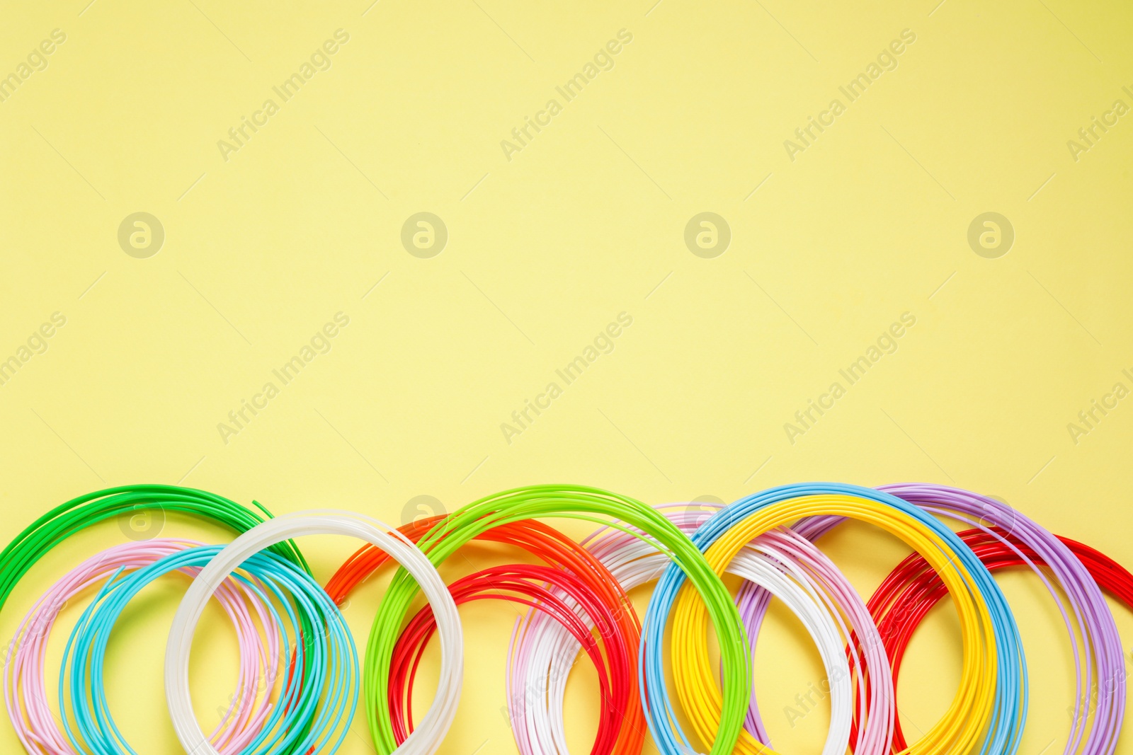 Photo of Colorful plastic filaments on pale yellow background, flat lay. Space for text