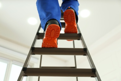 Professional worker climbing up ladder indoors, low angle view