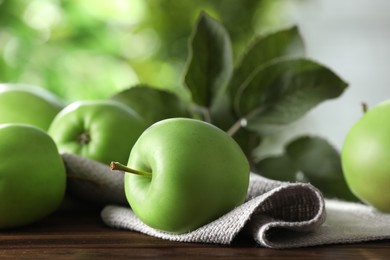 Fresh ripe green apples and leaves on wooden table outdoors, closeup