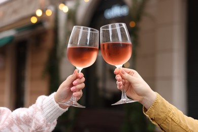 Women clinking glasses with rose wine outdoors, closeup