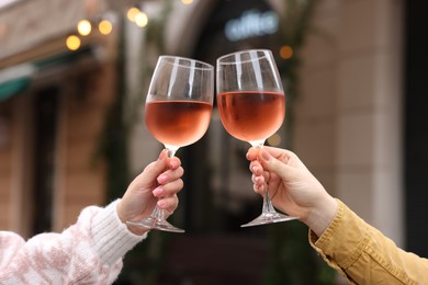 Photo of Women clinking glasses with rose wine outdoors, closeup