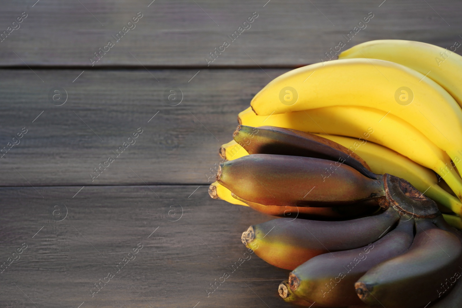 Photo of Tasty purple and yellow bananas on wooden table, space for text