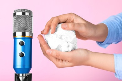 Photo of Woman making ASMR sounds with microphone and crumpled paper on pink background, closeup