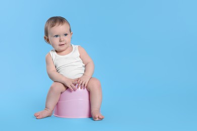 Photo of Little child sitting on baby potty against light blue background. Space for text