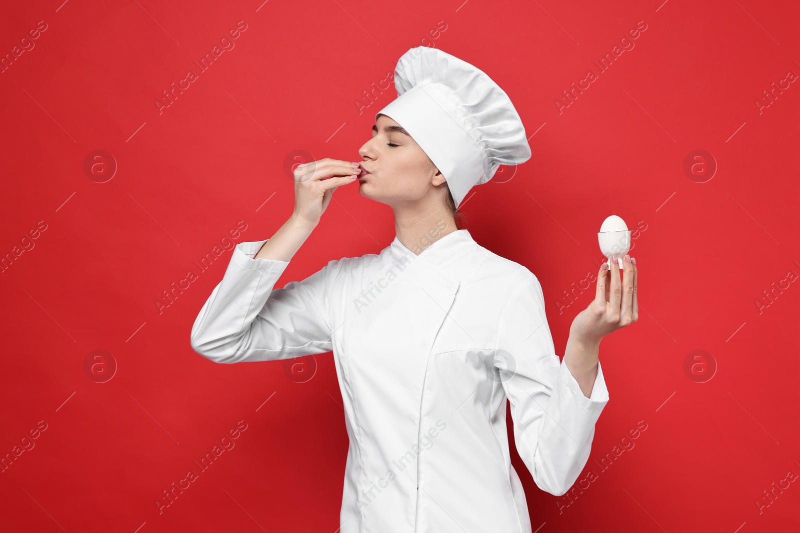 Photo of Professional chef holding egg and showing perfect sign on red background