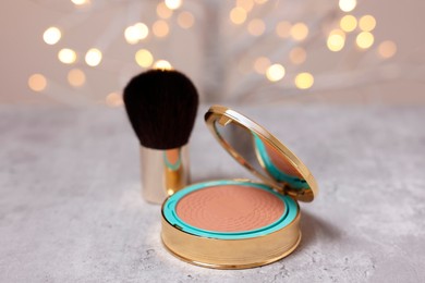 Face bronzer and makeup brush on grey textured table against blurred lights, closeup