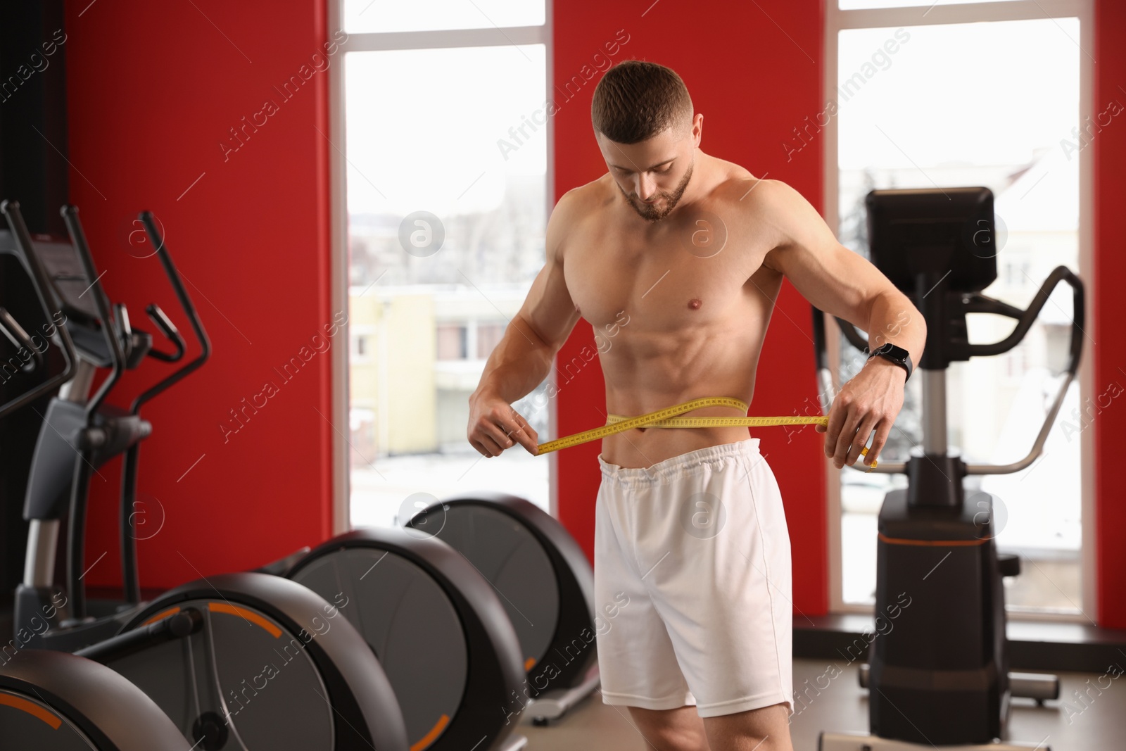 Photo of Athletic man measuring waist with tape in gym