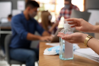 Photo of Office worker using hand sanitizer at table, closeup. Personal hygiene during COVID-19 pandemic