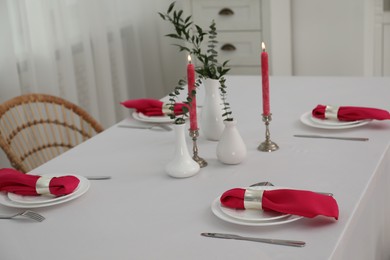 Beautiful table setting with green branches in vases and burning candles indoors. Stylish dining room