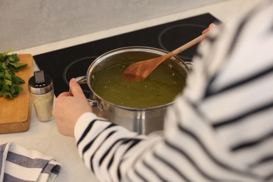 Photo of Woman with wooden spoon cooking soup in kitchen, closeup