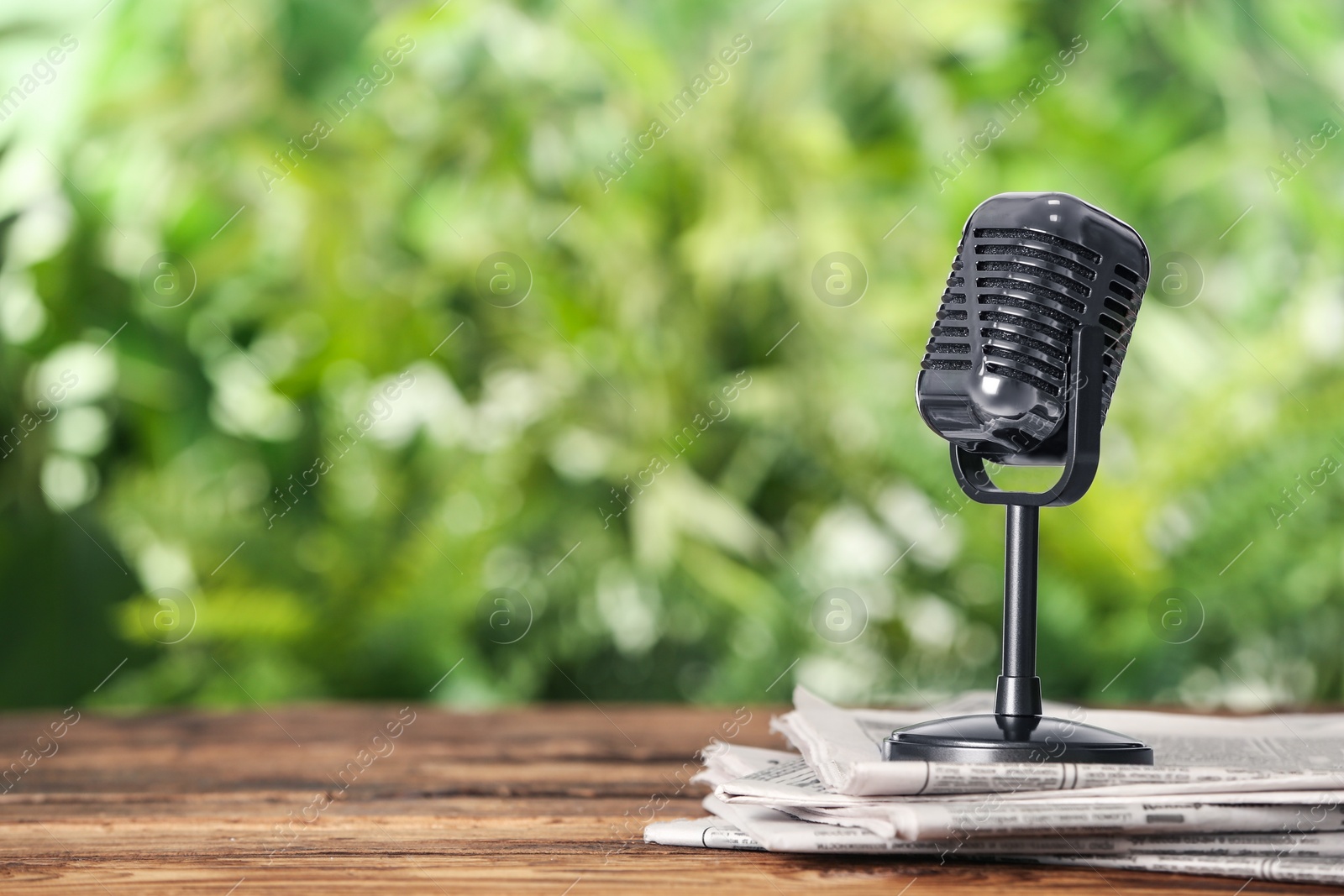 Photo of Newspapers and vintage microphone on wooden table against blurred green background, space for text. Journalist's work