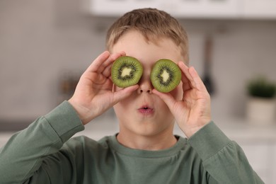 Photo of Funny boy covering eyes with halves of fresh kiwi indoors