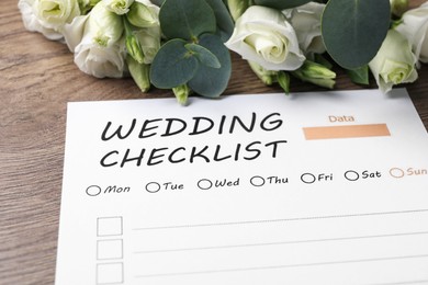 Photo of Wedding Checklist and flowers on wooden table, closeup