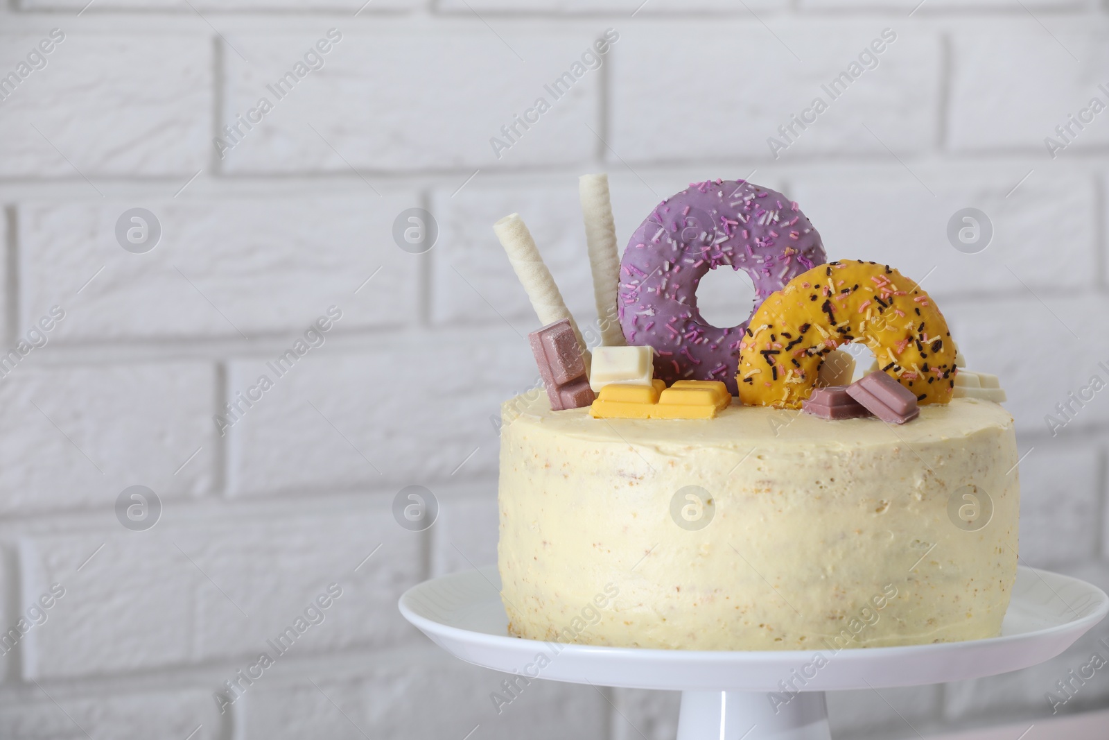 Photo of Delicious cake decorated with sweets near white brick wall, closeup. Space for text