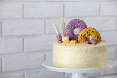 Photo of Delicious cake decorated with sweets near white brick wall, closeup. Space for text