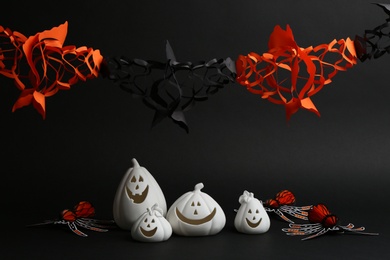 Photo of Jack-o-Lantern candle holders and festive garland on black background. Halloween decor