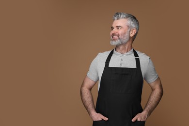 Photo of Happy man wearing kitchen apron on brown background. Mockup for design