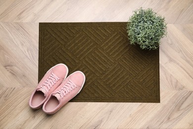 Stylish door mat, houseplant and shoes on wooden floor, top view