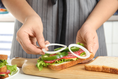 Photo of Woman adding onion to tasty sandwich at white wooden table, closeup