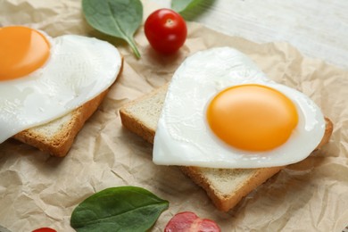 Heart shaped fried eggs with toasts, spinach and tomatoes on white wooden table, closeup