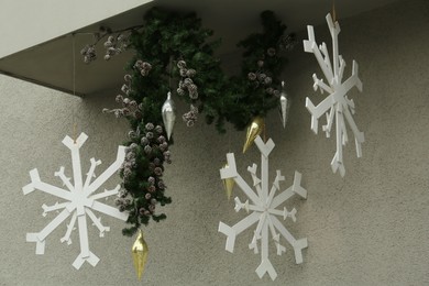 Photo of Beautiful Christmas snowflakes and green tree branches near light grey wall outdoors. Festive street decorations