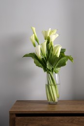 Beautiful calla lily flowers in vase on wooden commode