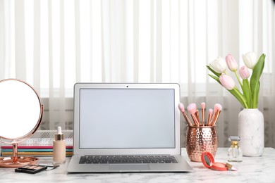 Photo of Laptop with blank screen, makeup products and beautiful flowers on white marble table indoors. Space for text