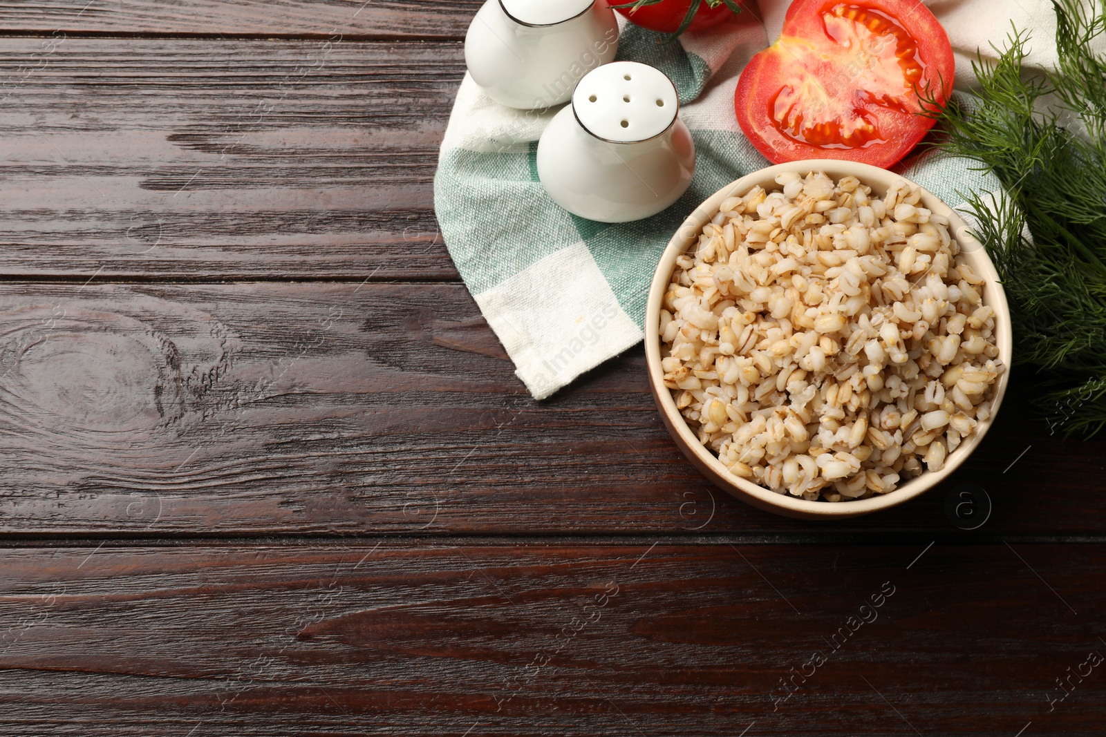 Photo of Delicious pearl barley in bowl served on wooden table, top view. Space for text