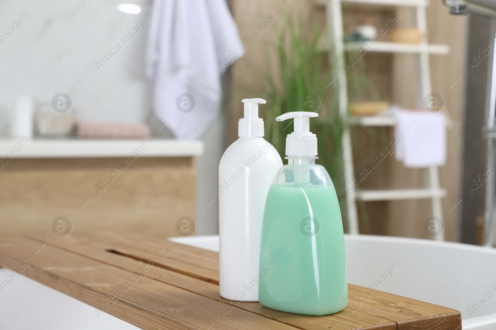 Photo of Wooden bath tray with bottles of shower gels on tub indoors, space for text