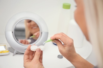 Senior woman taking contact lens from container in front of mirror