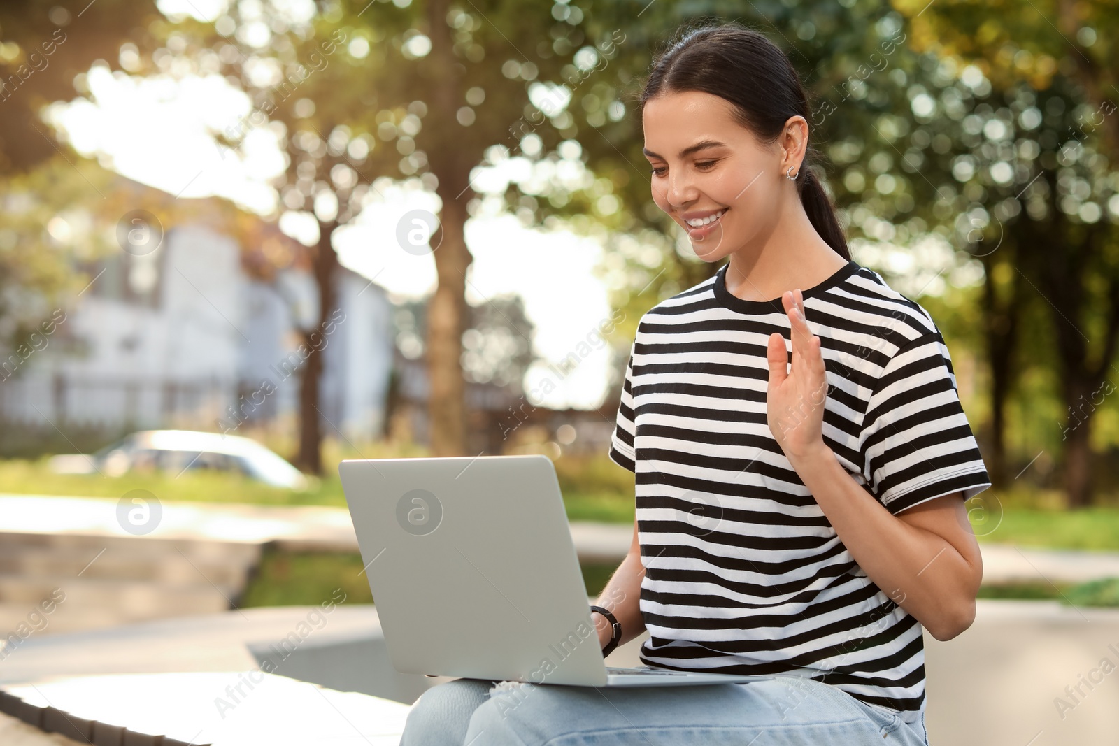 Photo of Happy young woman using modern laptop for video call outdoors. Space for text