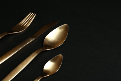 Photo of Set of gold cutlery on black background. Space for text
