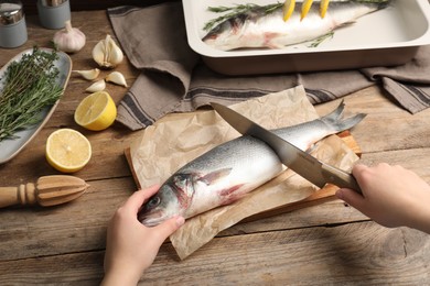 Woman cutting raw sea bass fish at wooden table, closeup