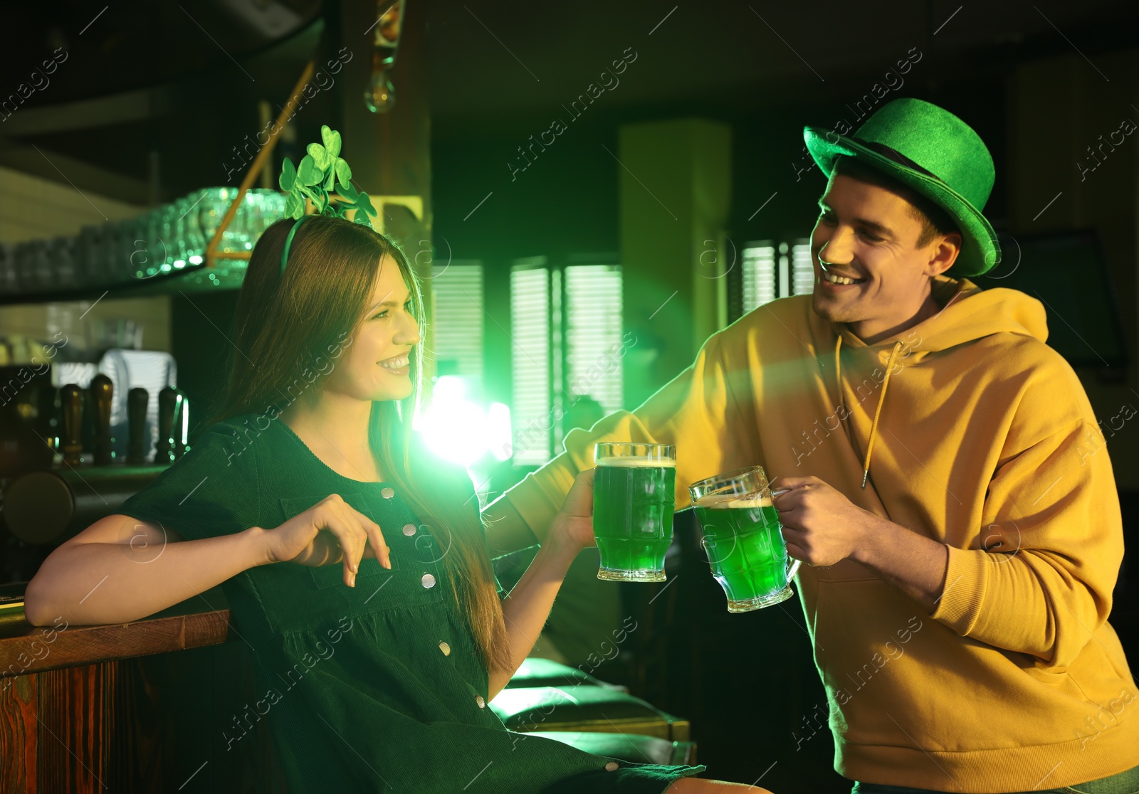 Photo of Young woman and man toasting with green beer in pub. St. Patrick's Day celebration