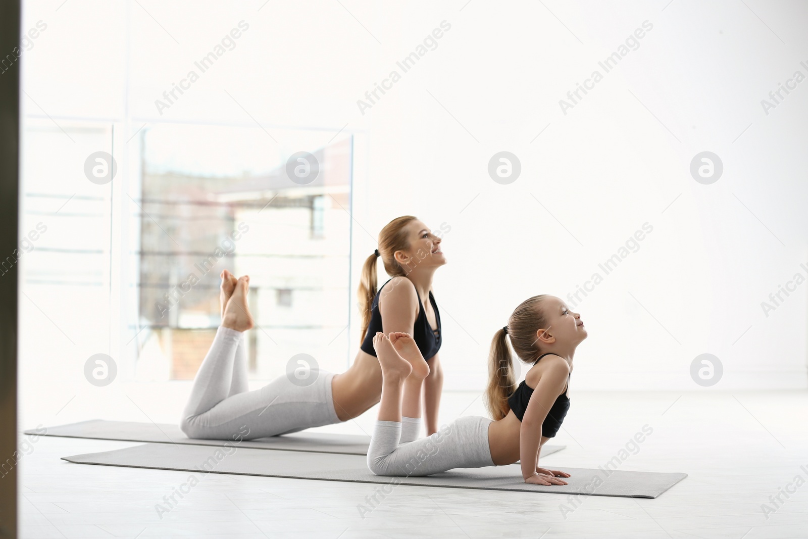 Photo of Mother and daughter in matching sportswear doing yoga together at home