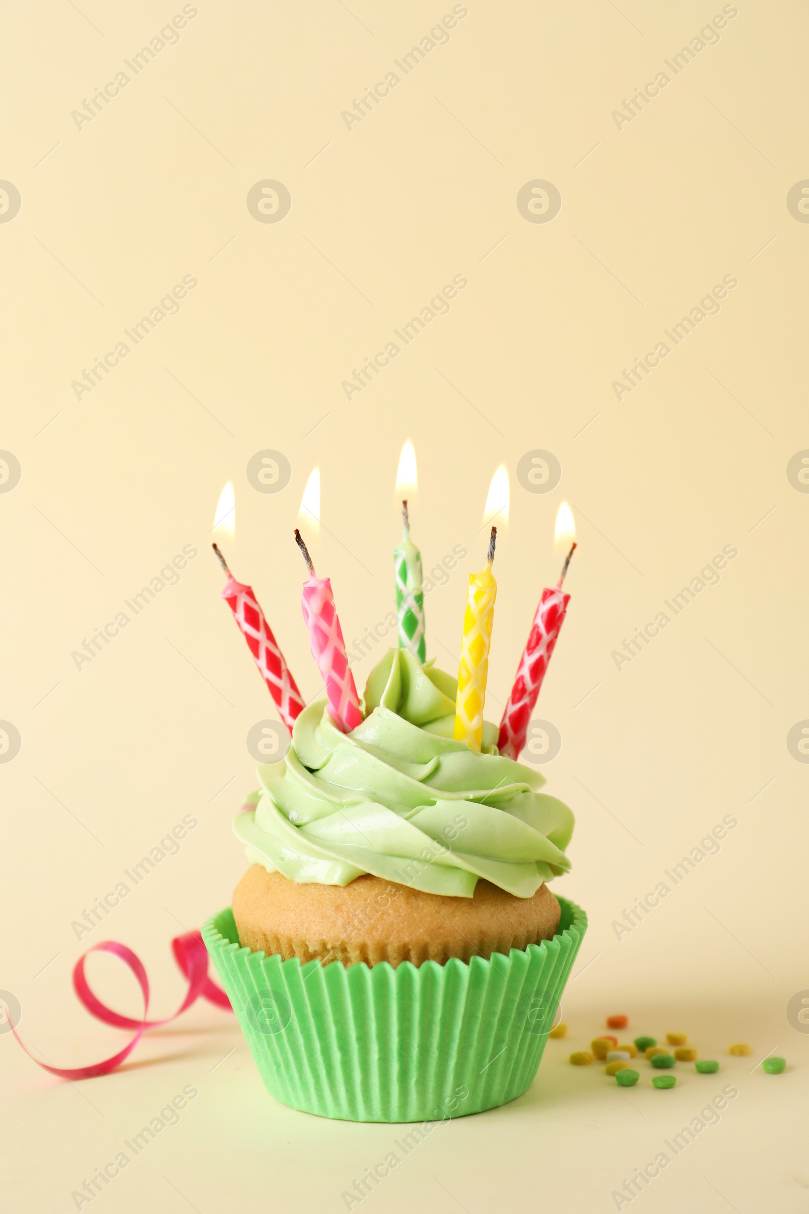 Photo of Birthday cupcake with burning candles, streamer and sprinkles on beige background